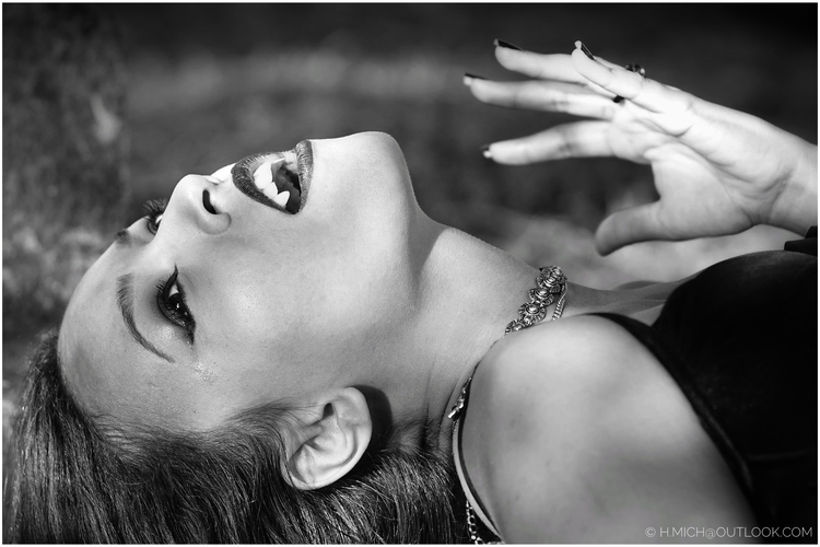 Diarium.Studio-One.Art.Br A black and white image of a person lying down with their head tilted back. They have dark nail polish, lipstick, and a choker necklace. The lighting highlights their facial features and the texture of their hair. (c) H.Mich