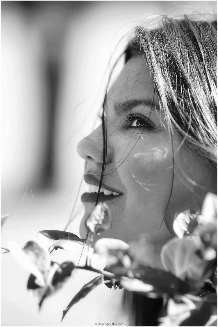 Diarium.Studio-One.Art.Br Black and white portrait of a woman gazing upwards, with a gentle smile. Her hair falls softly across her face, and she is framed by leaves in the foreground. (c) H.Mich