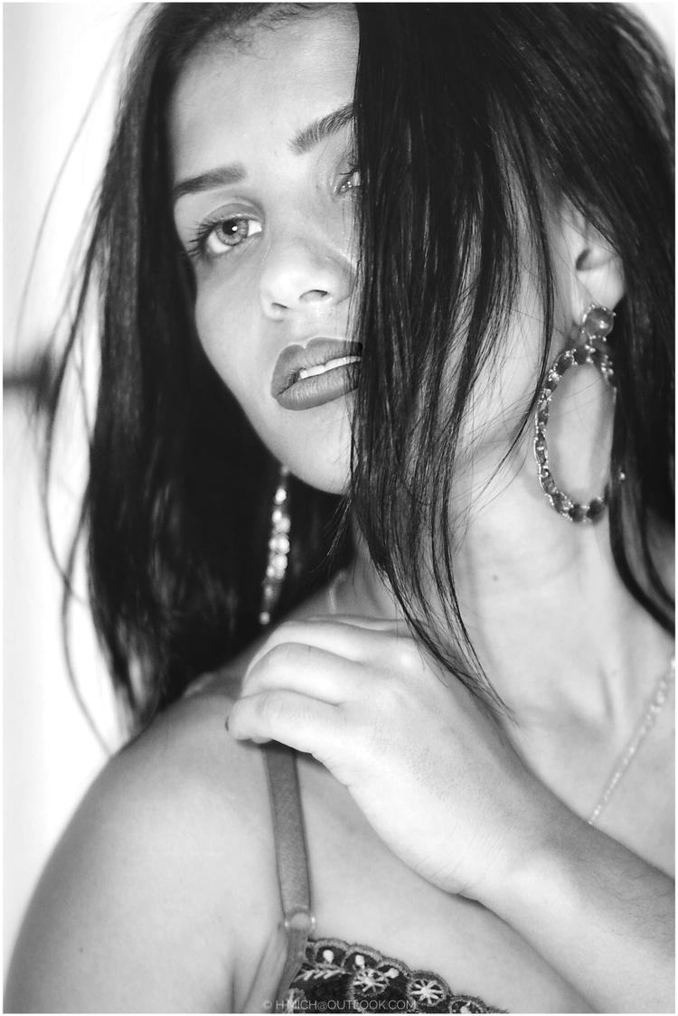 Diarium.Studio-One.Art.Br Black and white portrait of a woman with long dark hair partially covering her face. She has hoop earrings and a thoughtful expression, her hand gently touching her shoulder strap. (c) H.Mich
