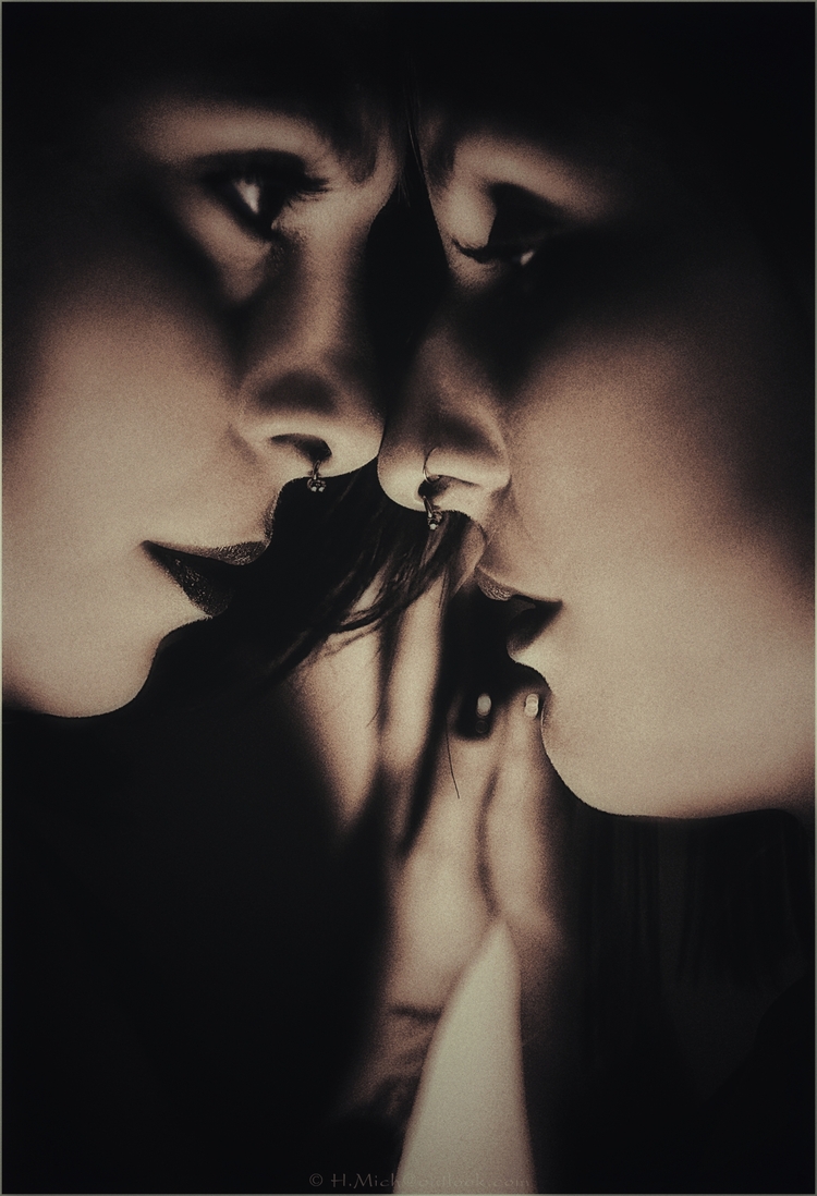 Diarium.Studio-One.Art.Br Close-up of two people in profile, facing each other intimately. One whispers to the other, who listens intently. The image is in sepia tone, highlighting shadows and expressions. Both have facial piercings. (c) H.Mich
